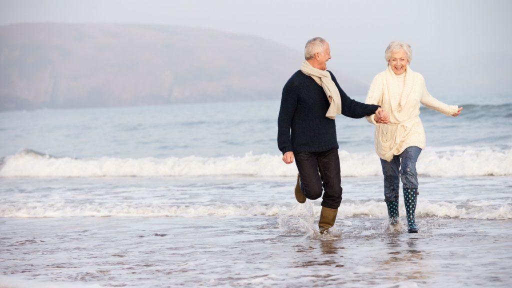 An older couple running through the sea laughing