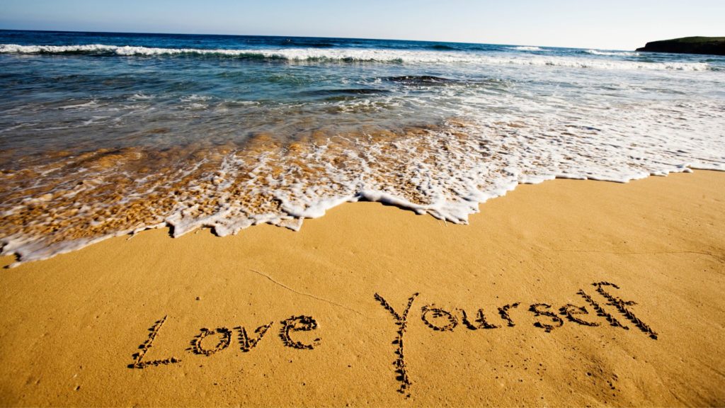 Image of a beach with love yourself written in the sand
